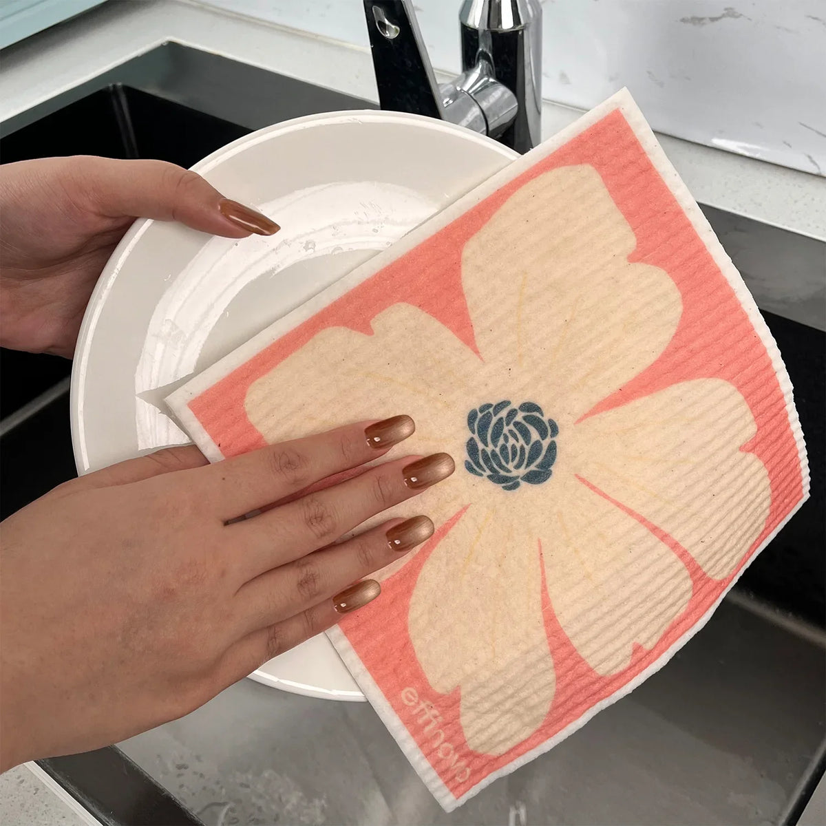 Eco-friendly floral dishcloth cleaning a white plate by a kitchen sink