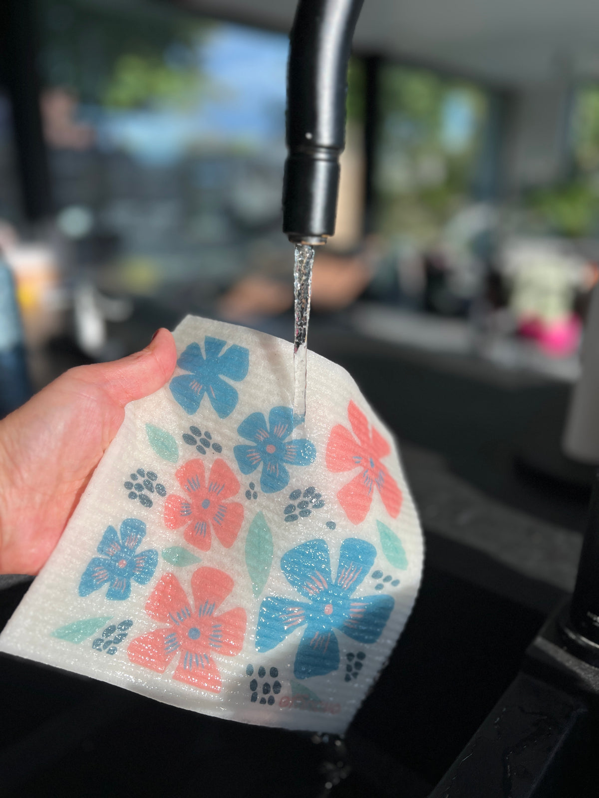 Hand rinsing eco-friendly reusable dishcloth with floral print under kitchen faucet
